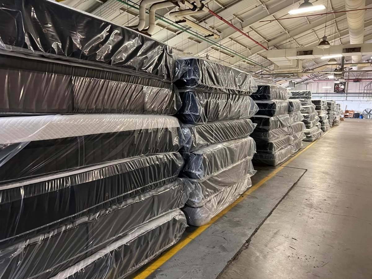 Rows of new mattresses wrapped in plastic, stacked in a warehouse
