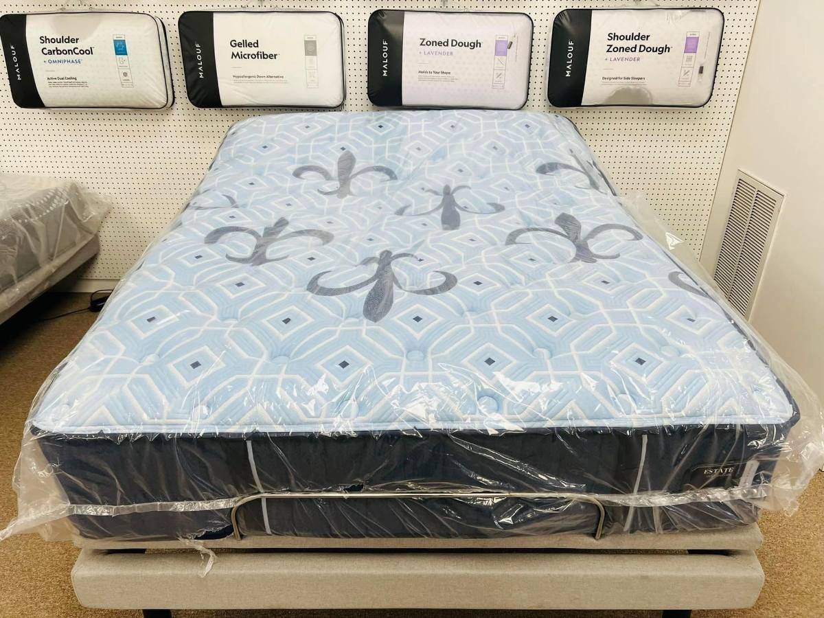 Mattress with a light blue quilted top on an adjustable base, with packaged pillows on the wall behind it