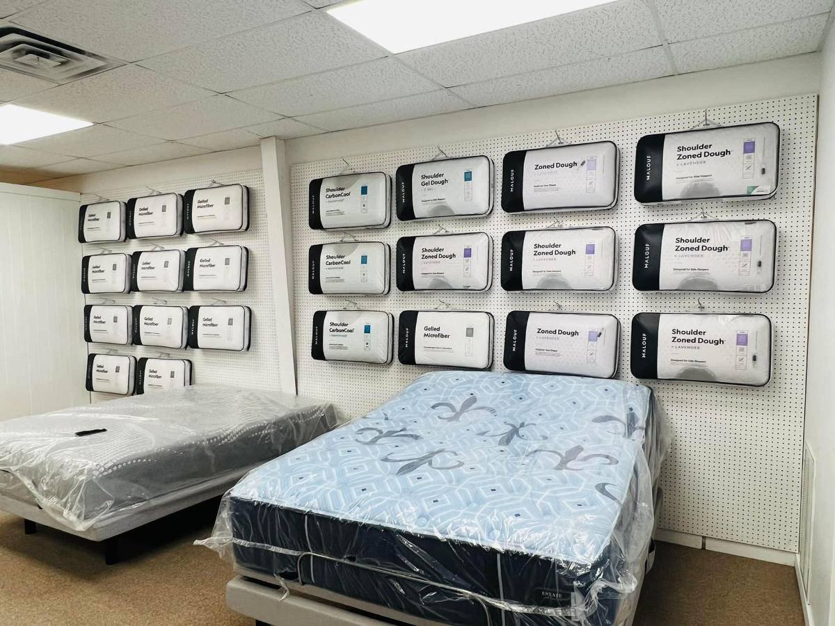 Wall of packaged pillows on pegboard above two mattresses wrapped in plastic